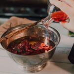 Hand Pouring Red Liquid in Stainless Steel Bowl